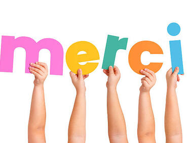 French Immersion hands raised holding the word Merci